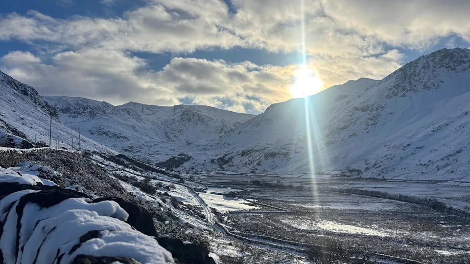 تشرق الشمس فوق أحد الوادي في ويلز، وترتفع الجبال المغطاة بالثلوج على كلا الجانبين