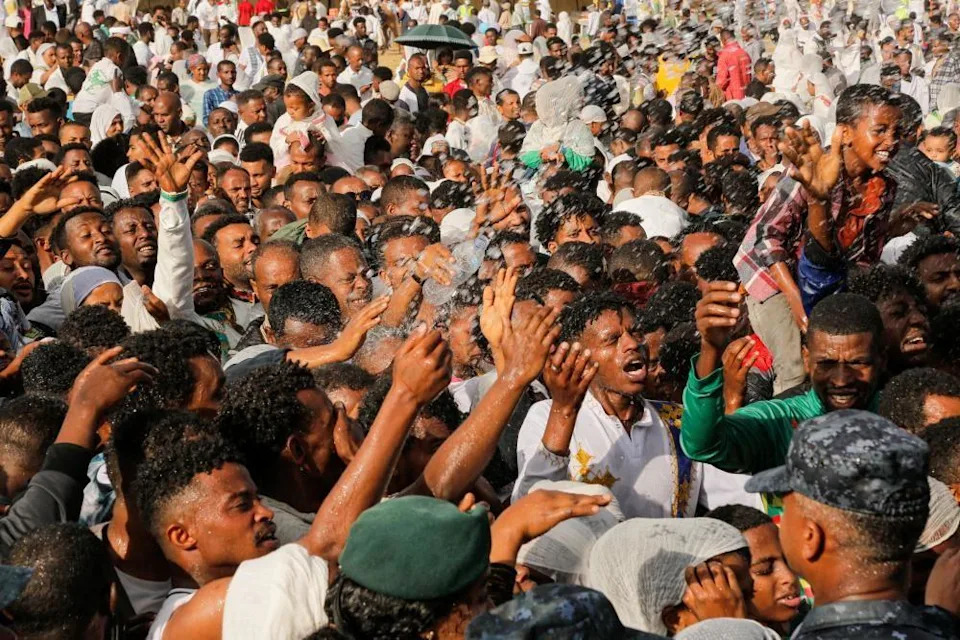 حشد كبير من المصلين يرفعون أيديهم أثناء رشهم بالماء في معمودية رمزية. 