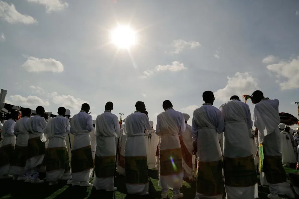 صورة مأخوذة من الخلف لمسيحيين أرثوذكس إثيوبيين يحتفلون بتيمكيت - وهم يرتدون ملابسهم الدينية التقليدية. يمكن رؤية الشمس الساطعة في السماء أعلاه.