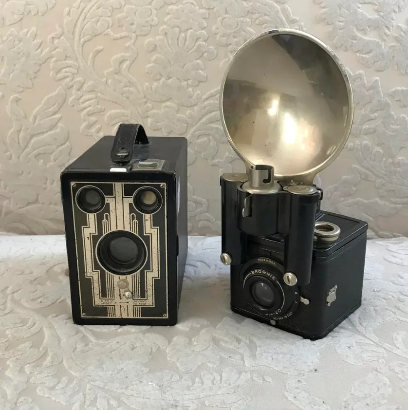 كاميرتان صندوقيتان عتيقتان، إحداهما بتصميم آرت ديكو والأخرى بملحق فلاش كبير، مثبتتان على سطح مزخرف