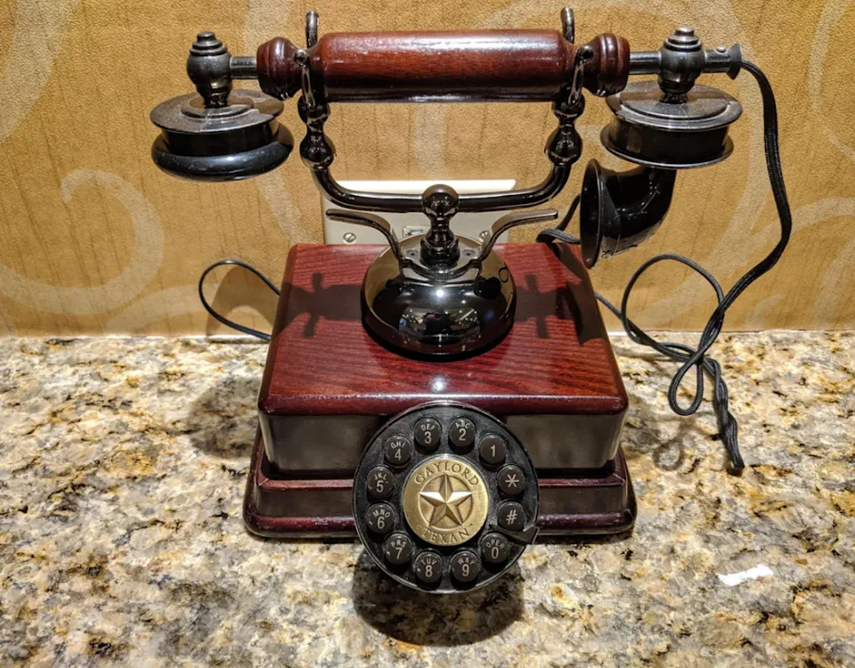 هاتف دوار عتيق بقاعدة خشبية ولمسات نحاسية على سطح رخامي