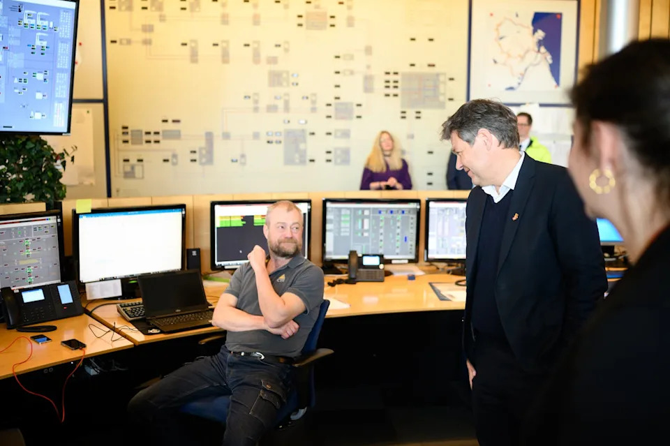 يتحدث الناس في غرفة بها العديد من شاشات الكمبيوتر ورسوم بيانية كبيرة على الحائط.