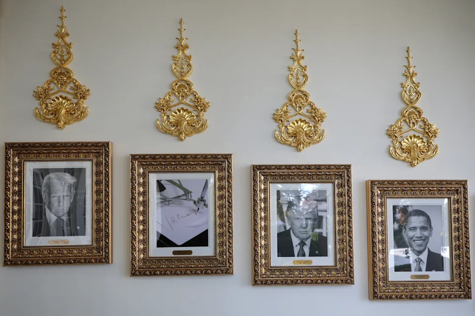 أربع صور مؤطرة معلقة على الحائط، كل منها تصور رئيسًا أمريكيًا: ترامب وبايدن وأوباما وصورة طائرة. زخارف ذهبية مزخرفة فوق كل إطار