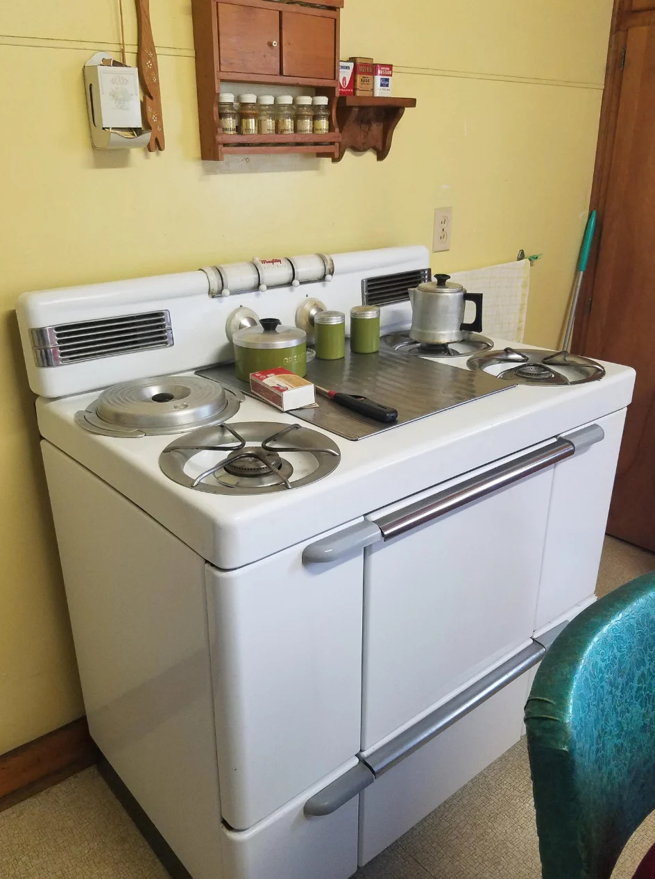 مطبخ عتيق به موقد كلاسيكي ورف توابل بالأعلى وأجهزة صغيرة. يظهر الجدول جزئيًا على اليمين