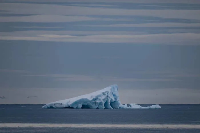 جبل جليدي يطفو في بحر هادئ تحت سماء ملبدة بالغيوم، مما يوضح قضايا البيئة وتغير المناخ