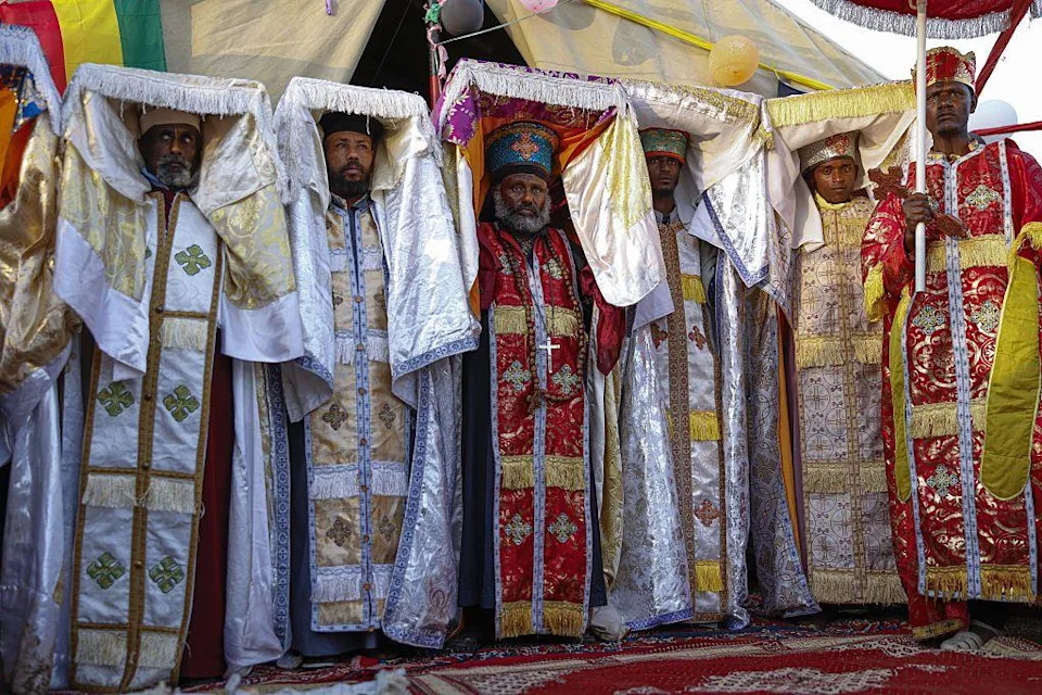 مجموعة من الكهنة يرتدون ملابس تقليدية يرفعون الجزء العلوي من أثوابهم الملونة فوق رؤوسهم.