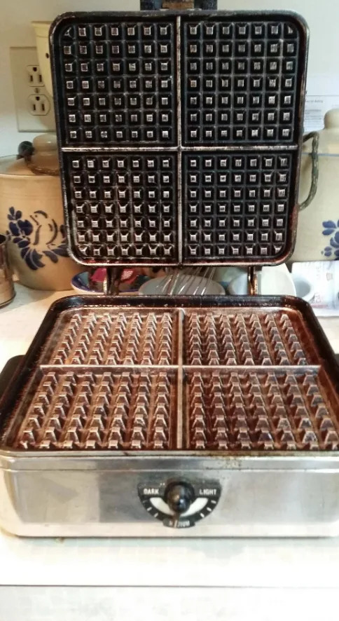 افتح مكواة الوافل على طاولة المطبخ مع وجود علامة على مقبض التحكم المرئي "مظلم" و "ضوء." عناصر المطبخ المختلفة موجودة في الخلفية