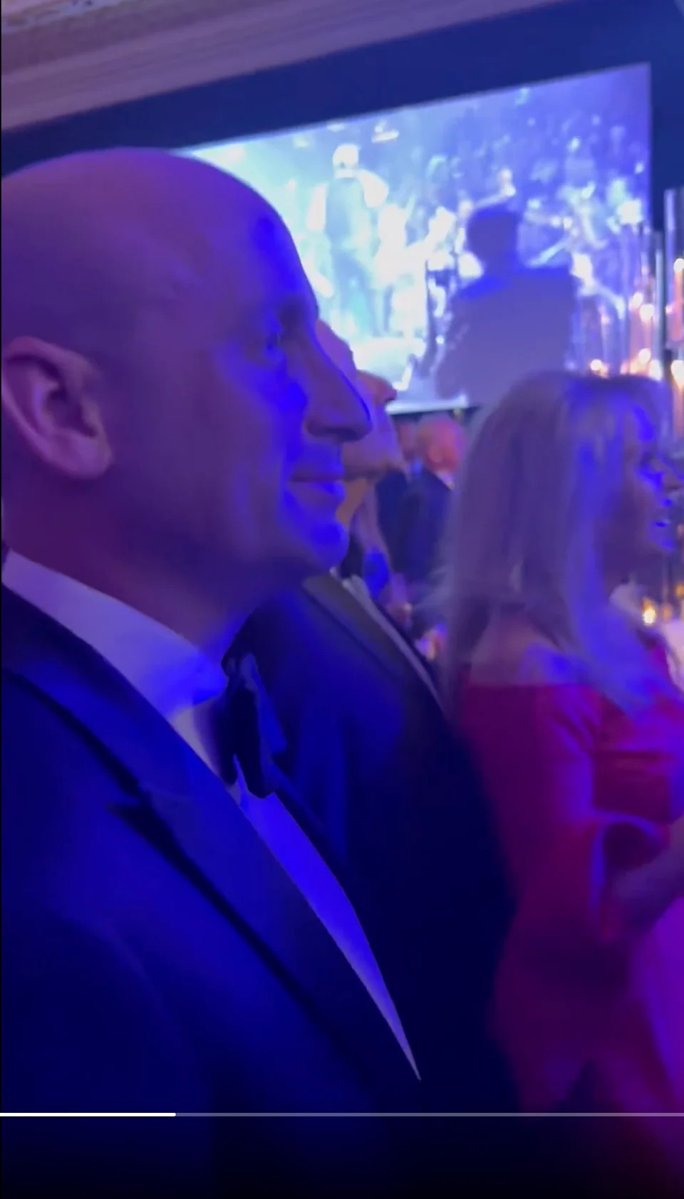 رجل يرتدي بدلة رسمية وامرأة ترتدي فستانًا أحمر أنيقًا يشاهدان عرضًا حيًا في حدث داخلي