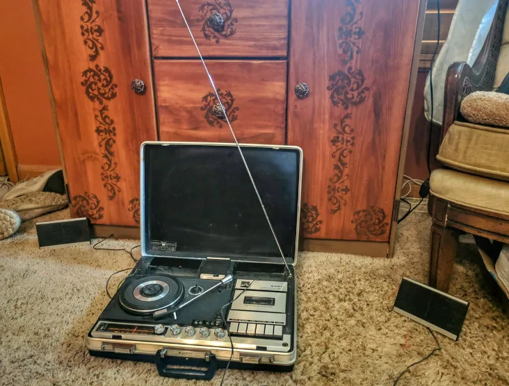 قرص دوار محمول عتيق مزود بسماعات مدمجة على أرضية مغطاة بالسجاد، ومحاط بأثاث خشبي