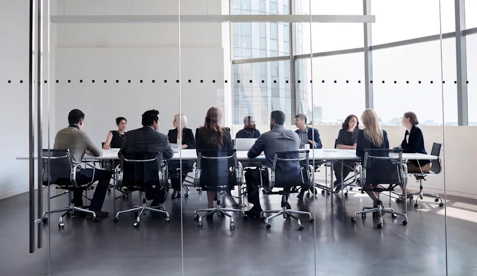 أشخاص يجلسون حول طاولة في غرفة الاجتماعات ويمكن رؤيتهم من خلال جدار زجاجي
