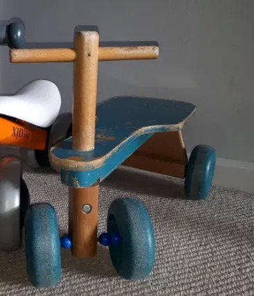 لعبتان للركوب للأطفال، بما في ذلك دراجة ثلاثية العجلات ودراجة توازن بأربع عجلات، موضوعة على أرضية مغطاة بالسجاد في الداخل