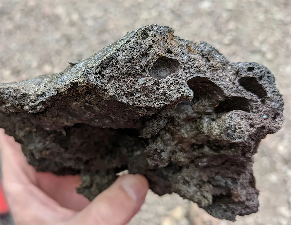 يتم رفع صخرة رمادية أمام الكاميرا، ويتم التركيز على بنيتها المسامية 