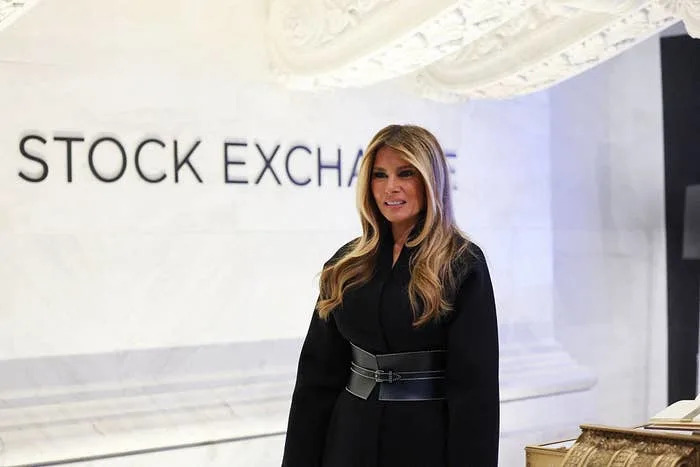 شخص يقف في البورصة، يرتدي زيًا أسود اللون، ويبتسم قليلاً. الإعداد رسمي ومهني