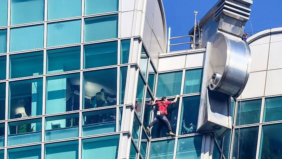 متسلق الصخور الأمريكي أليكس هونولد يتسلق مبنى تايبيه 101 بدون حبال أو معدات أمان. وهو يرتدي بنطالا أسود وقميصا أحمر. 