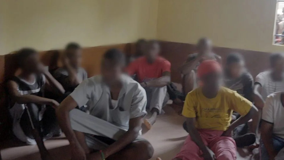 شباب وشابات يجلسون على الأرض، وجوههم غير واضحة. تم العثور عليهم في المنزل الذي داهمته الشرطة في ماكيني.