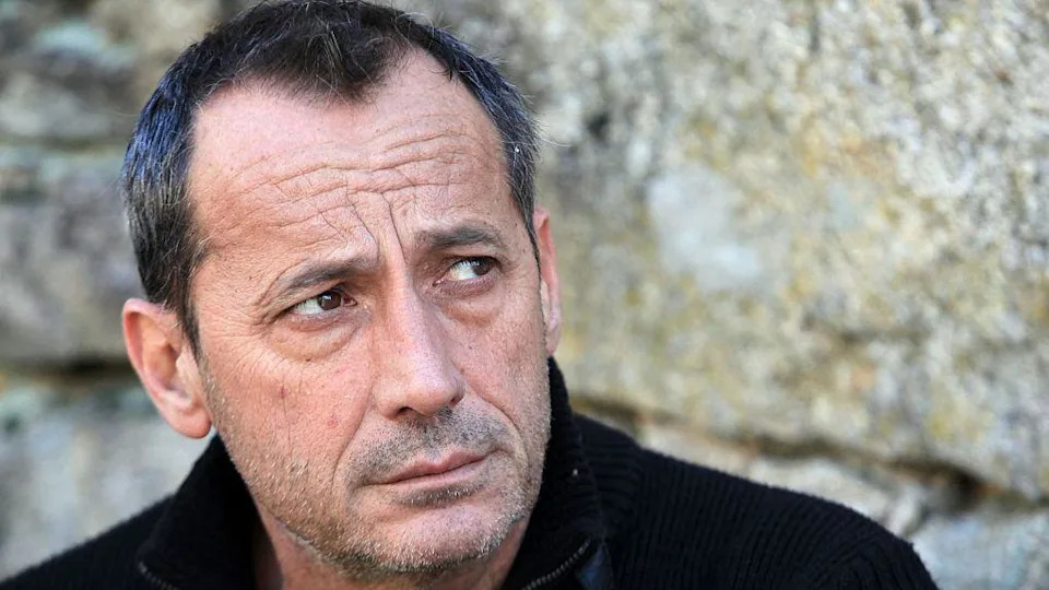 رجل يرتدي سترة سوداء يبدو مرتبكًا ولحية قصيرة وشعر رمادي