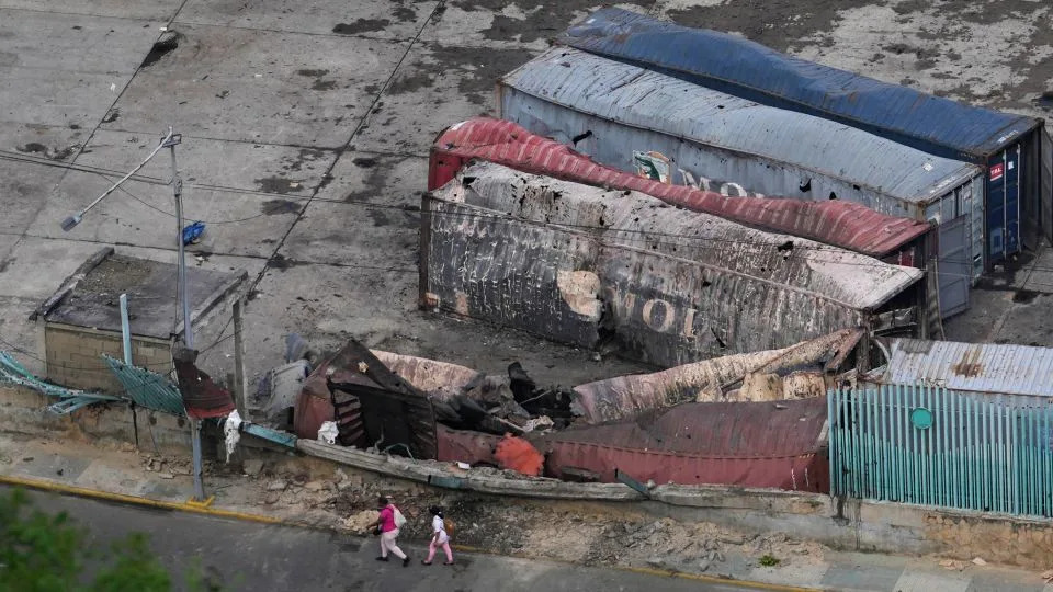 مشاة يسيرون بجوار الحاويات المدمرة في ميناء لا جويرا بعد سماع انفجارات في فنزويلا، السبت 3 يناير 2026. - ماتياس ديلاكروا / ا ف ب