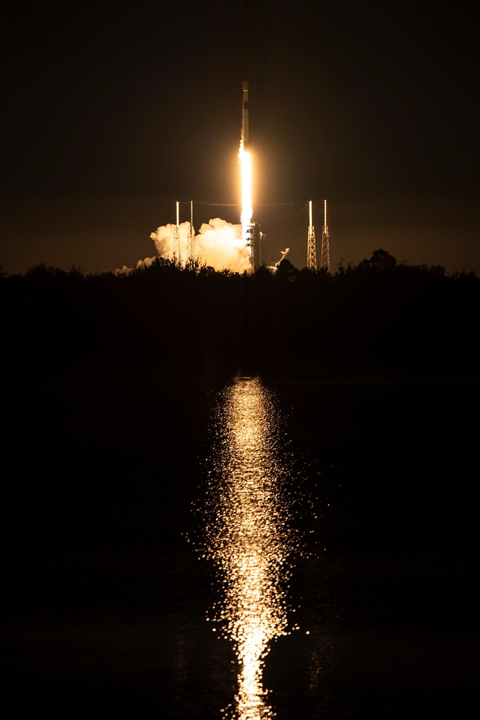 يظهر إطلاق ليلي لصاروخ مداري في الأفق وينعكس في جسم مائي في المقدمة