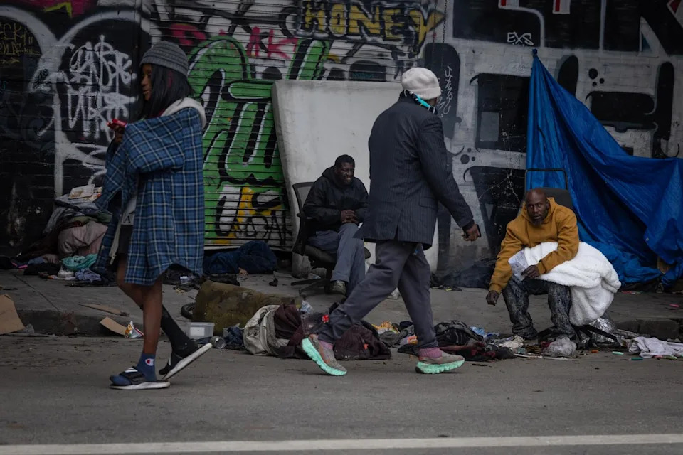 يسير الناس بجوار أشخاص مستلقين أو جالسين على الرصيف.