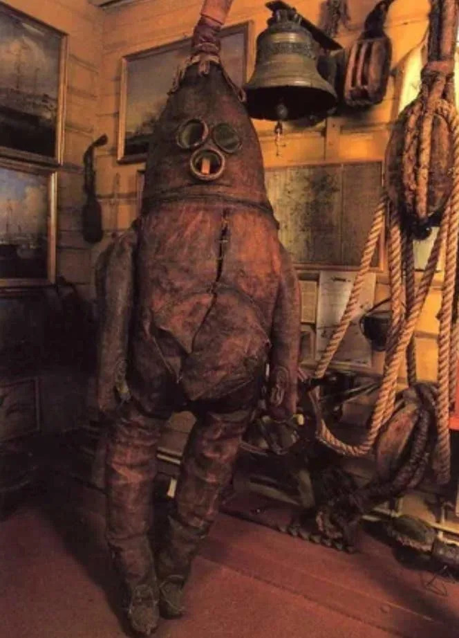 بدلة غوص عتيقة مع خوذة وخرطوم معروضة في غرفة ذات طابع بحري مع حبال ولوحات وجرس