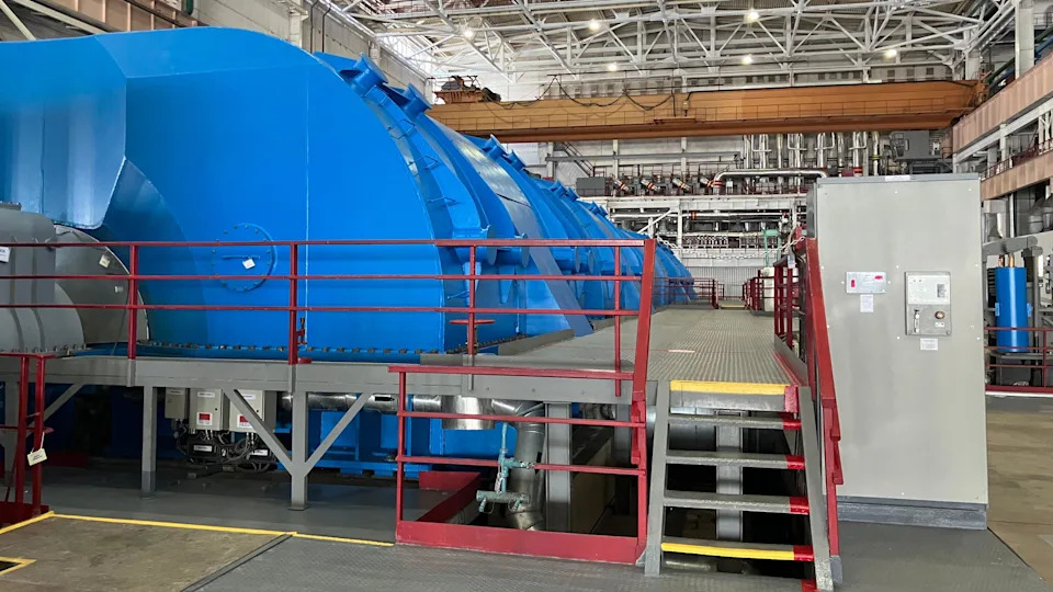 قاعة التوربينات في محطة الطاقة النووية. يوجد توربين أزرق عملاق في قاعة كبيرة، مع درجات تؤدي إليها.