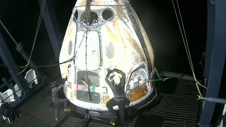 يتسلق شخصان يرتديان قبعات صلبة كبسولة بيضاء مخروطية الشكل على سطح بارجة في البحر