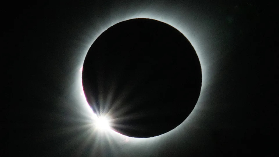 تظهر هالة متوهجة من الضوء تحيط بدائرة مظلمة مع كرة ساطعة من الضوء في أسفل اليسار أمام خلفية داكنة